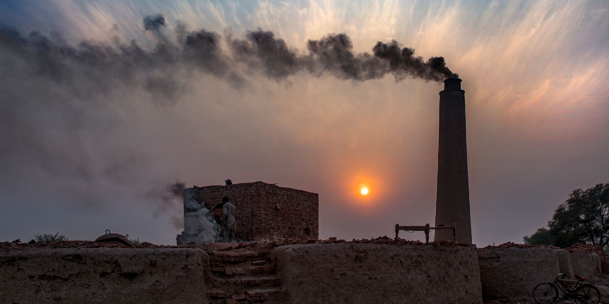 Kiln filling sky with dark smoke obscuring sun