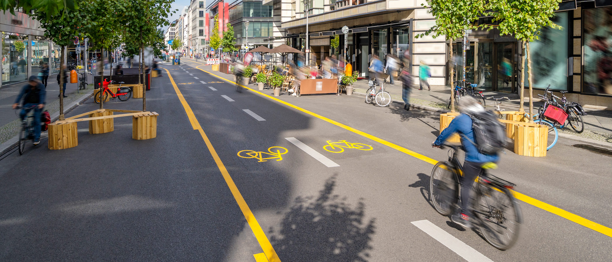 Commuter riding a bicycle in a two-direction bike lane on a pedestrian-friendly street in the shopping district of a downtown area.