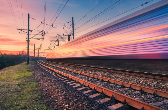 Fast-moving electric train on rural tracks at sunset.